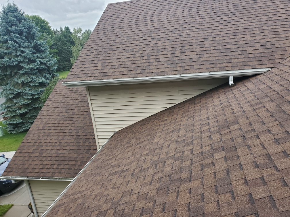 Brown shingle roof slopes meeting beside siding and white gutters