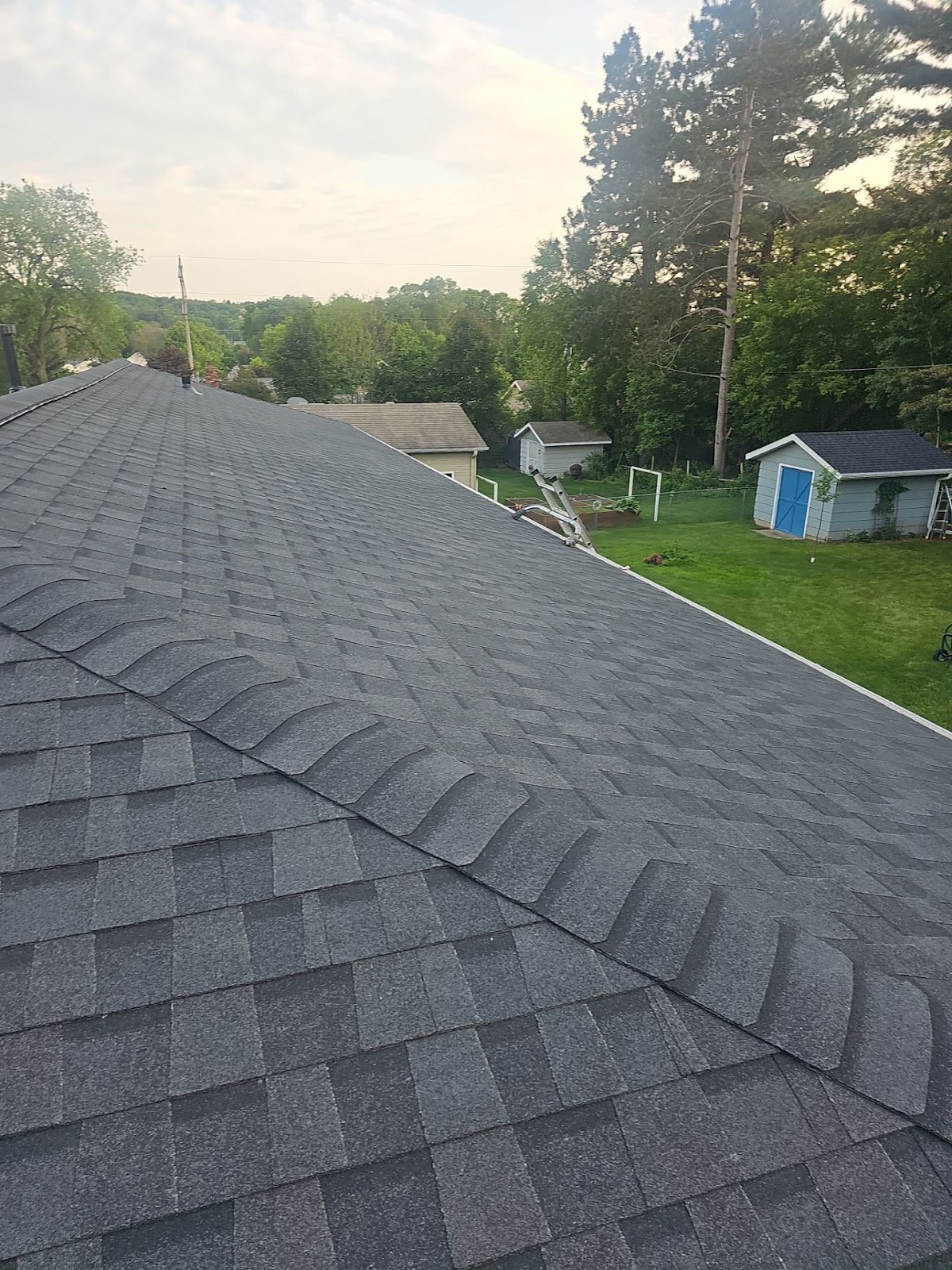 Long view along a completed gray shingle ridge above a residential yard