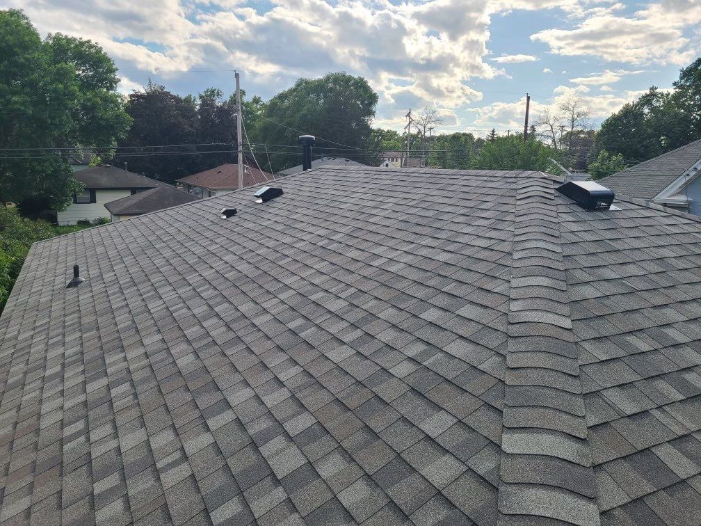 Wide view of a completed gray shingle roof with ridge caps and vents