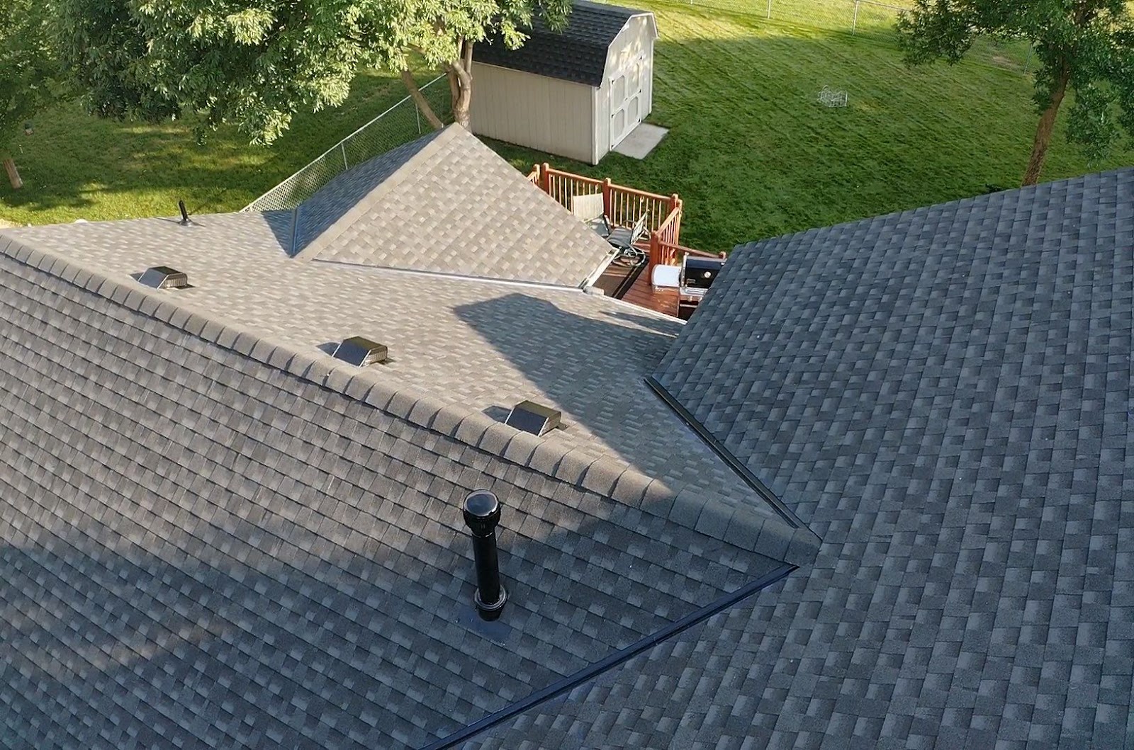 Elevated view of a finished gray shingle roof with valleys, vents, and chimney